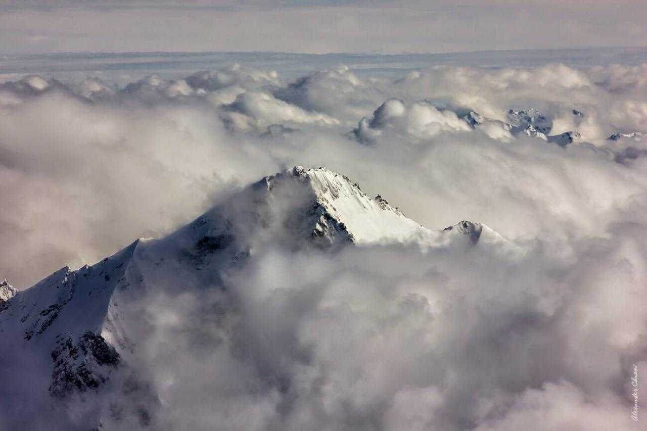 Горные вершины над облаками в снегу